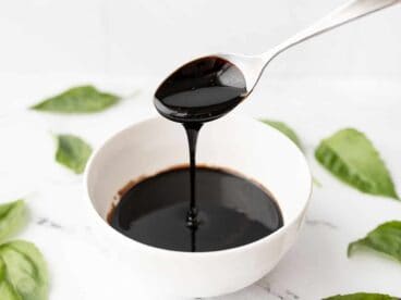 Balsamic glaze dripping off a spoon into a small dish, basil leaves all around