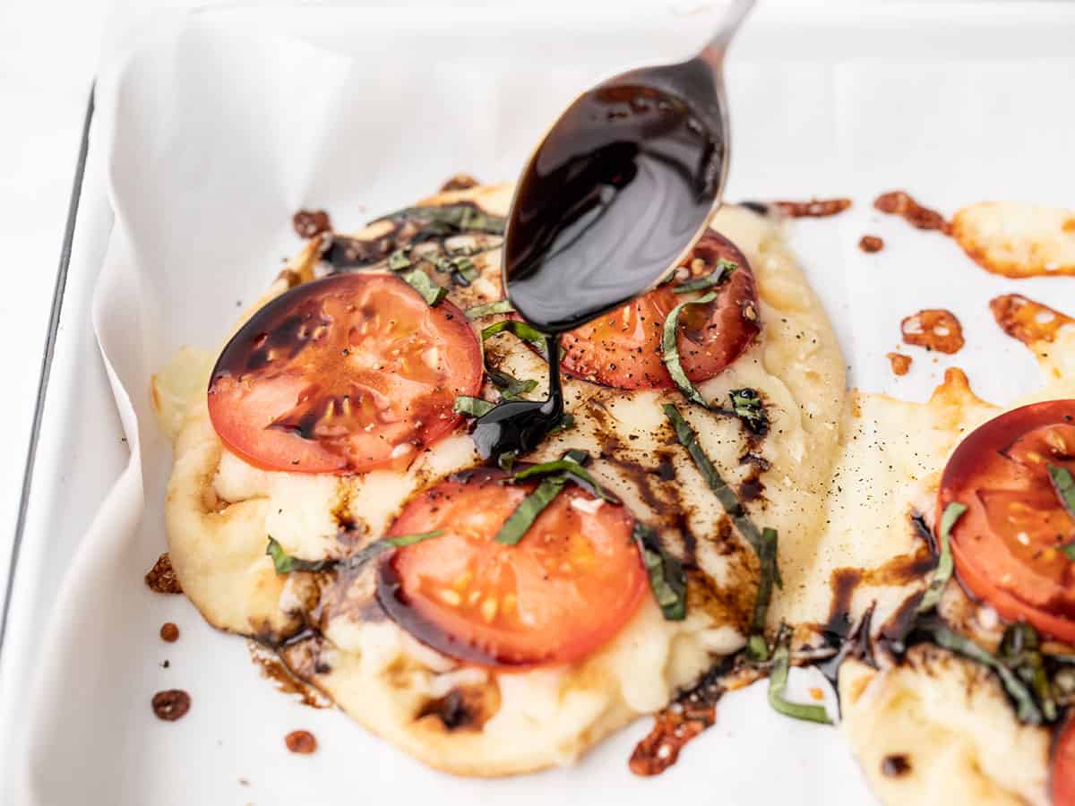 Balsamic glaze being drizzled onto a Caprese pizza