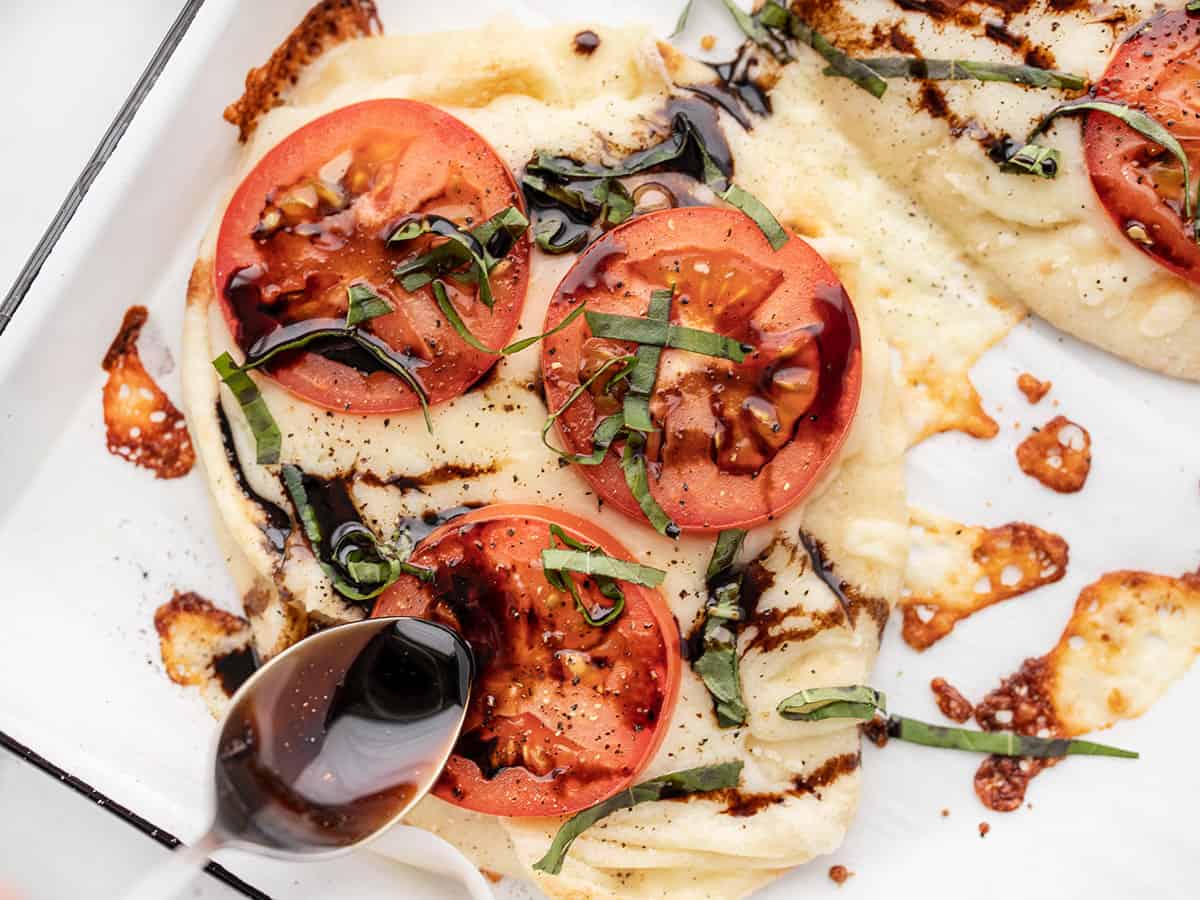 Balsamic glaze being drizzled over a Caprese pizza close up