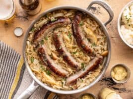 Bratwurst and sauerkraut in a skillet with beer, potatoes, and mustard on the sides