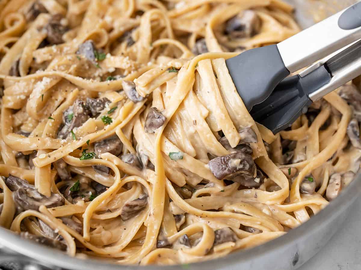 Close up of pasta being twirled around the tongs in the skillet