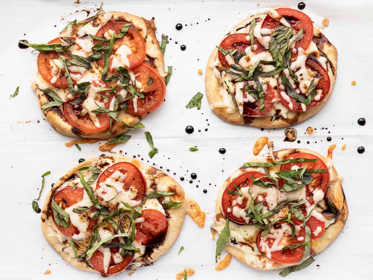 four finished caprese pizzas on a baking sheet