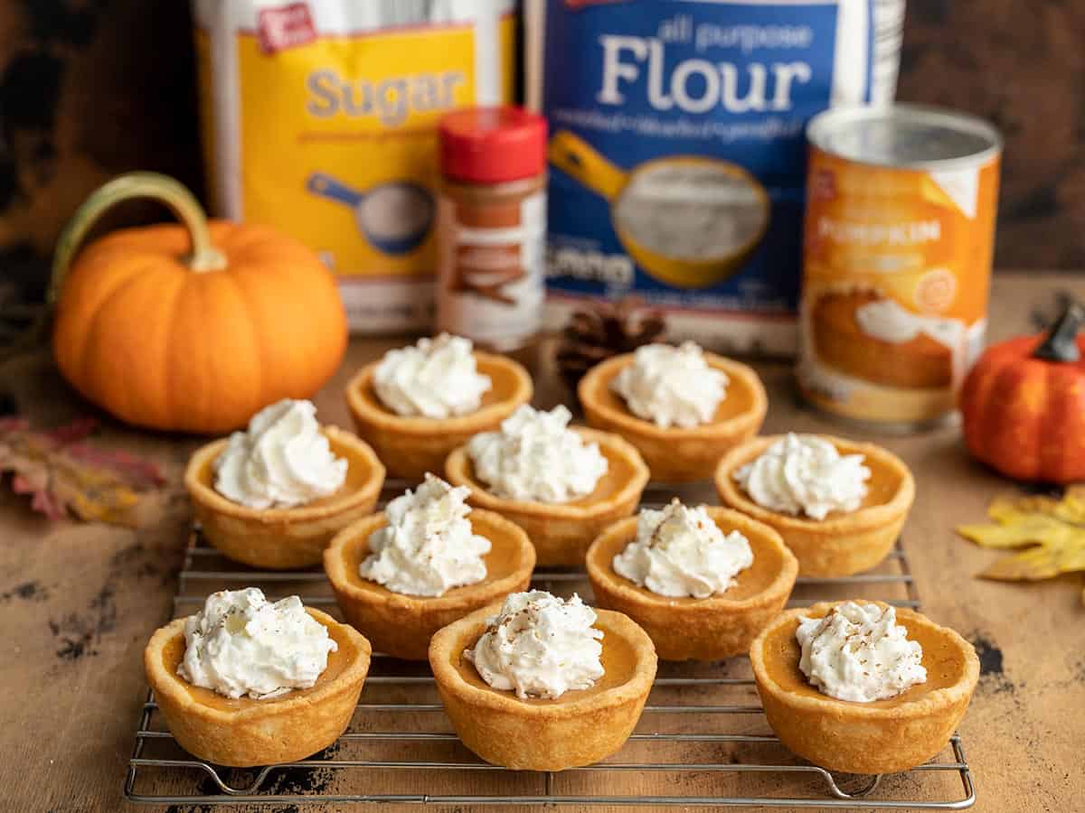 Mini pumpkin pies on a cooling rack with ingredients in the background