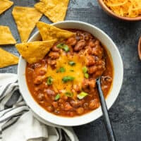 Overhead view of a bowl of pumpkin chili with cheese and tortilla chips