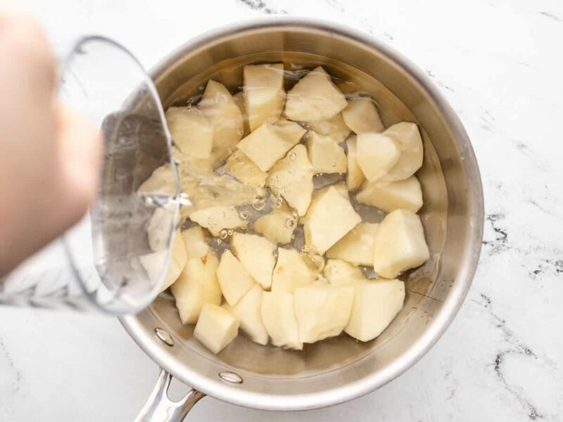 Water being poured over cubed potatoes in a pot