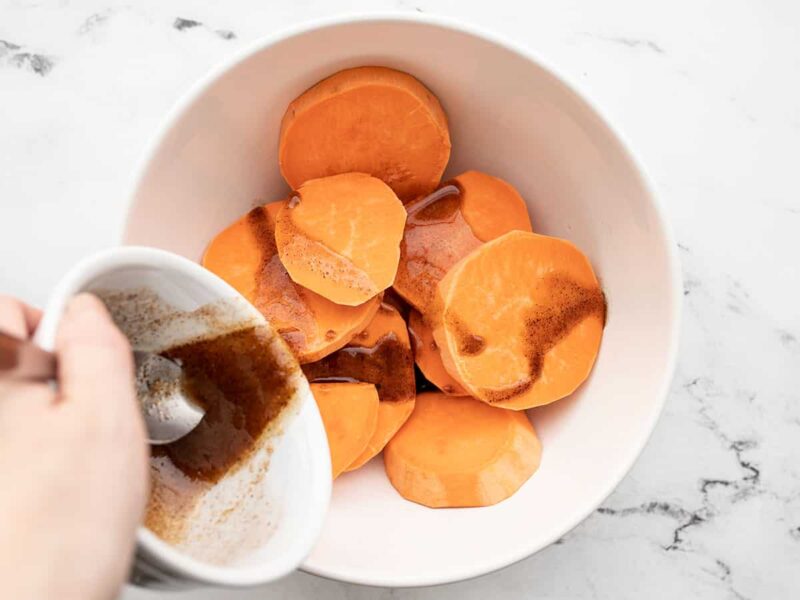Sweet butter being poured over sweet potato rounds in a bowl