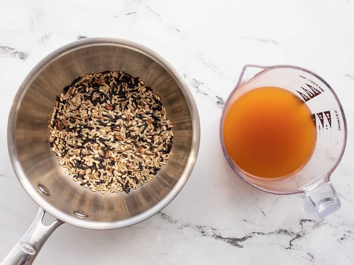 wild rice in the pot next to a measuring cup with vegetable broth