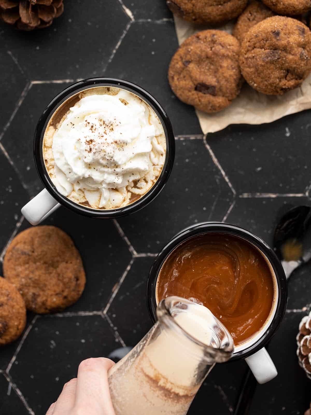 Overhead view of two cups of coffee with creamer being poured into one