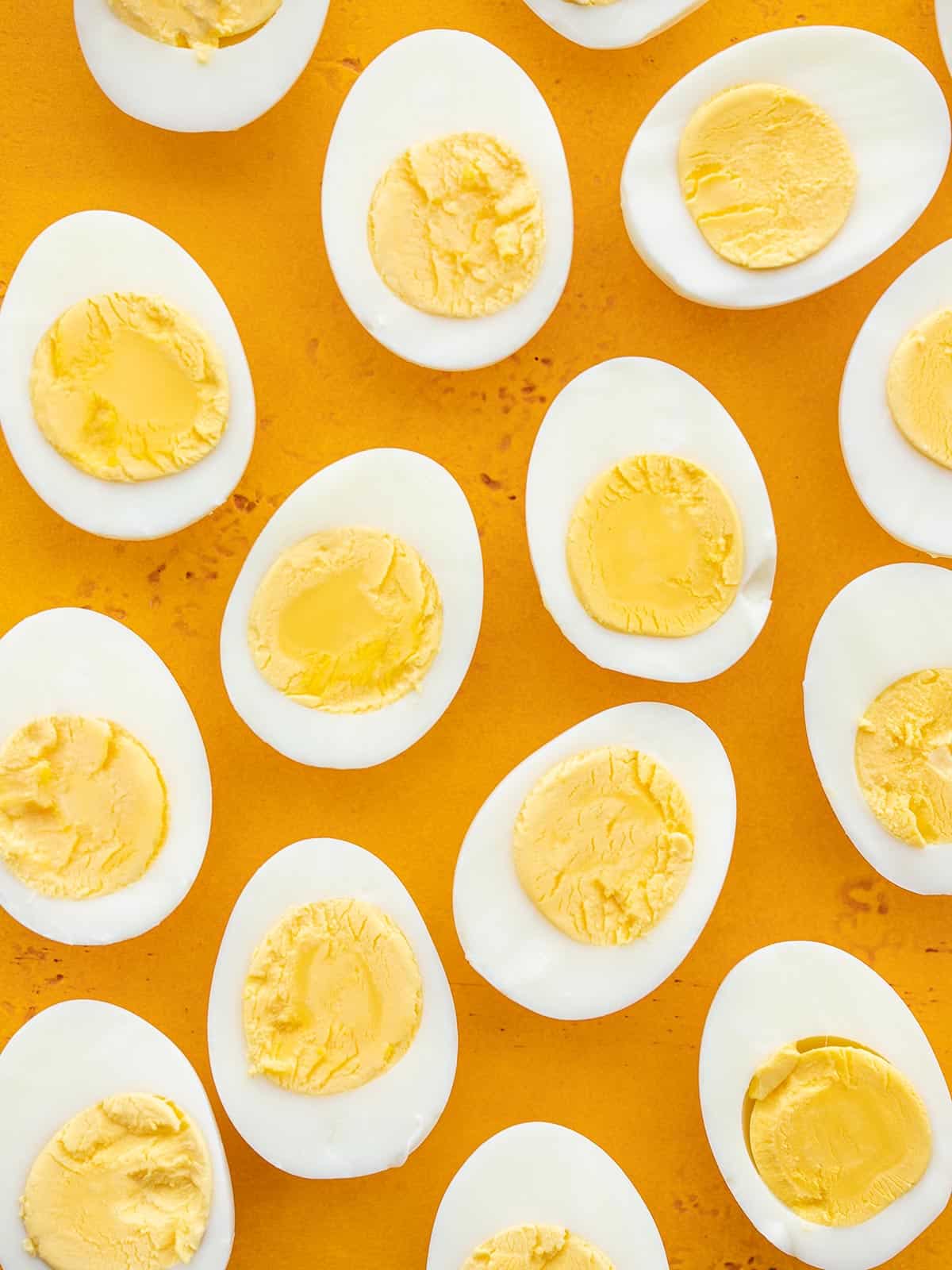 Several hard boiled eggs cut in half against a yellow background