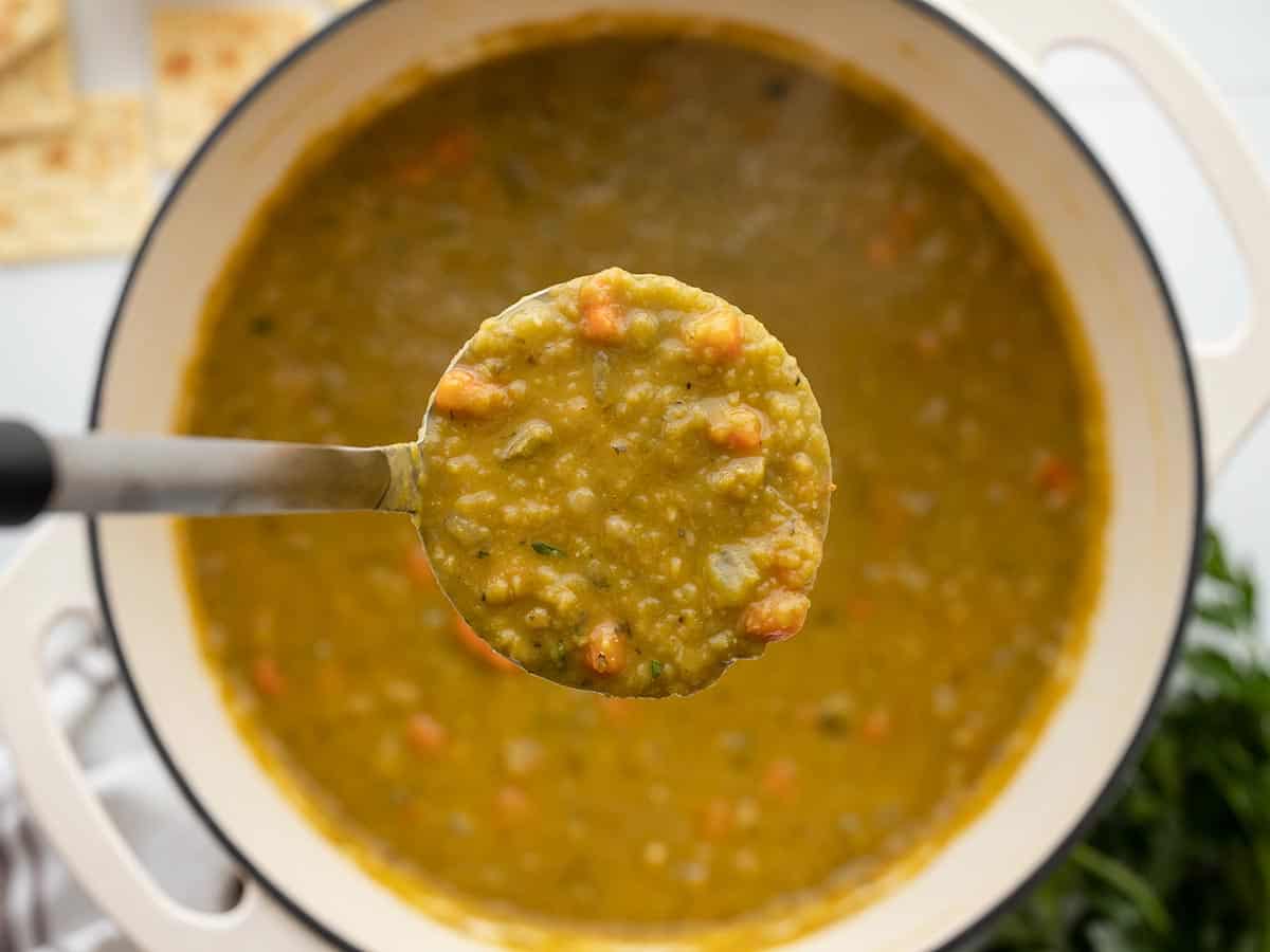 Close up of a ladle full of split pea soup held over the pot