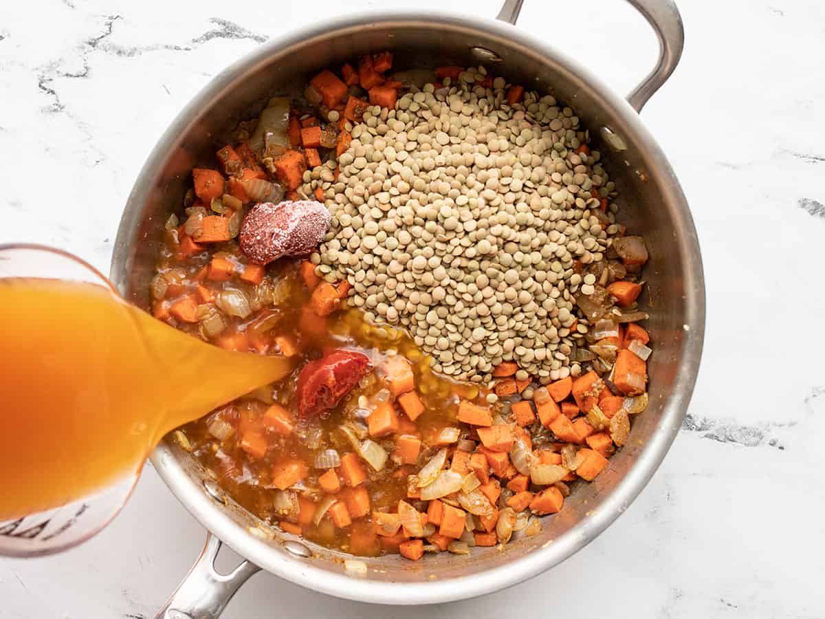 lentils, tomato paste, and broth being added to the skillet