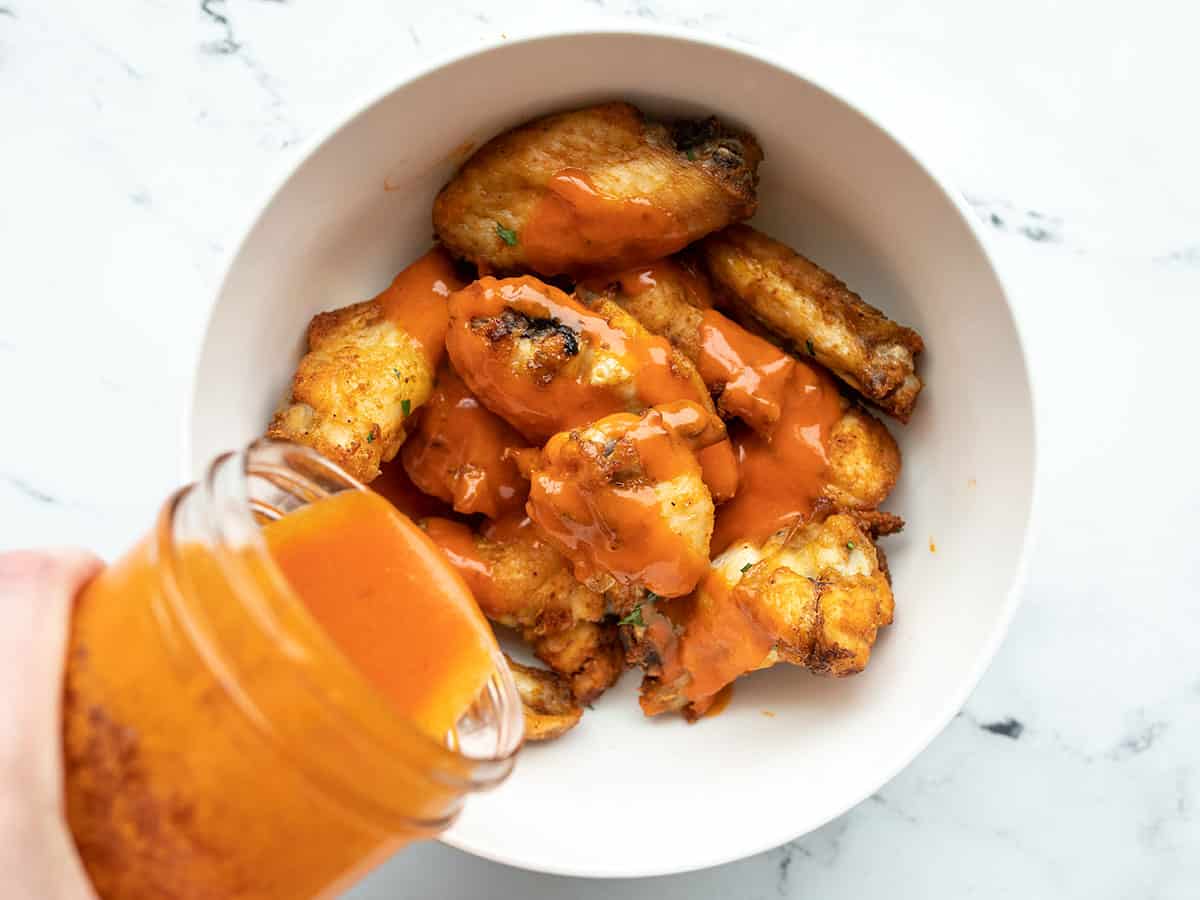 buffalo sauce being poured over a bowl of chicken wings