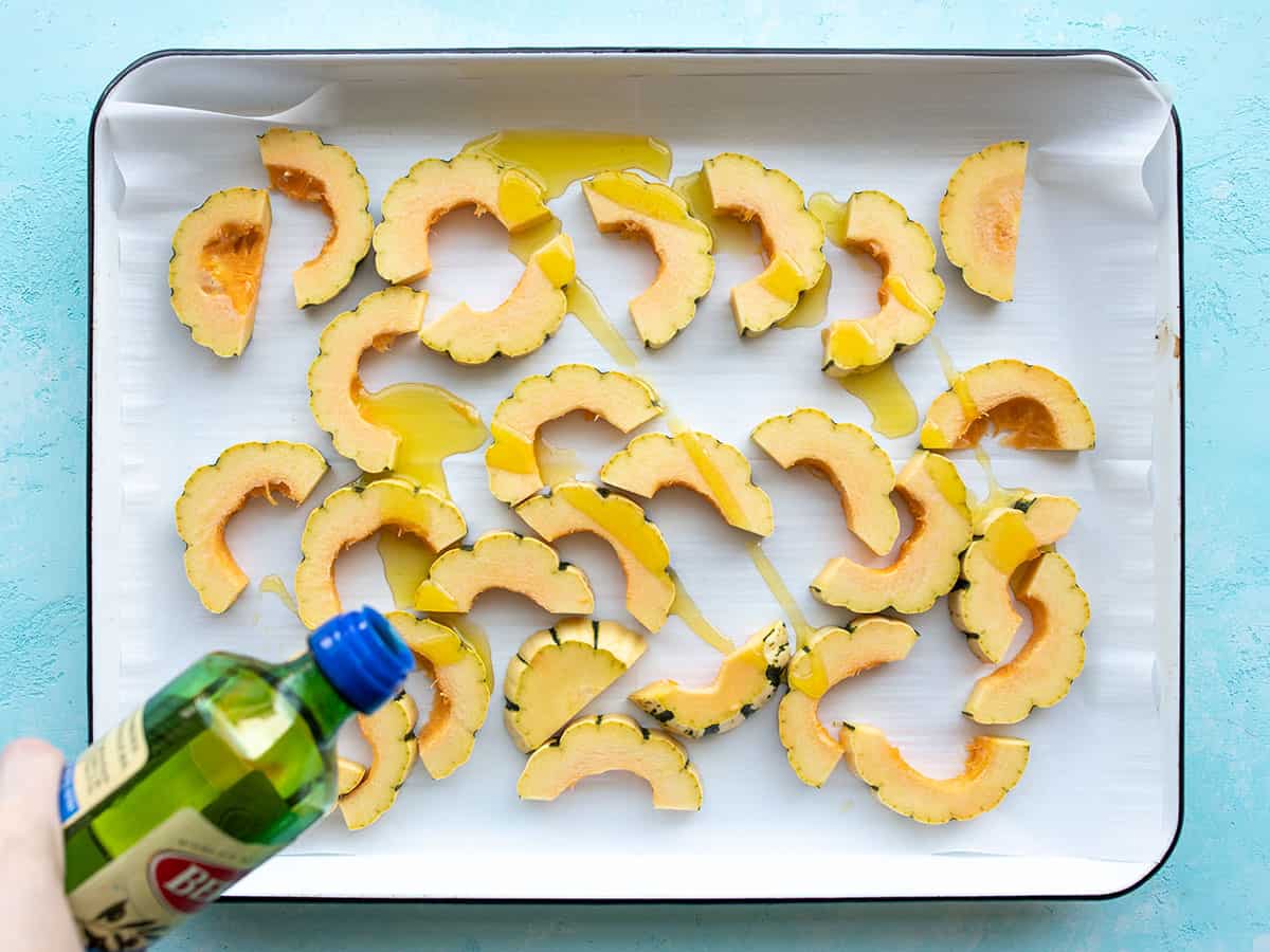 squash slices on a baking sheet being drizzled with oil