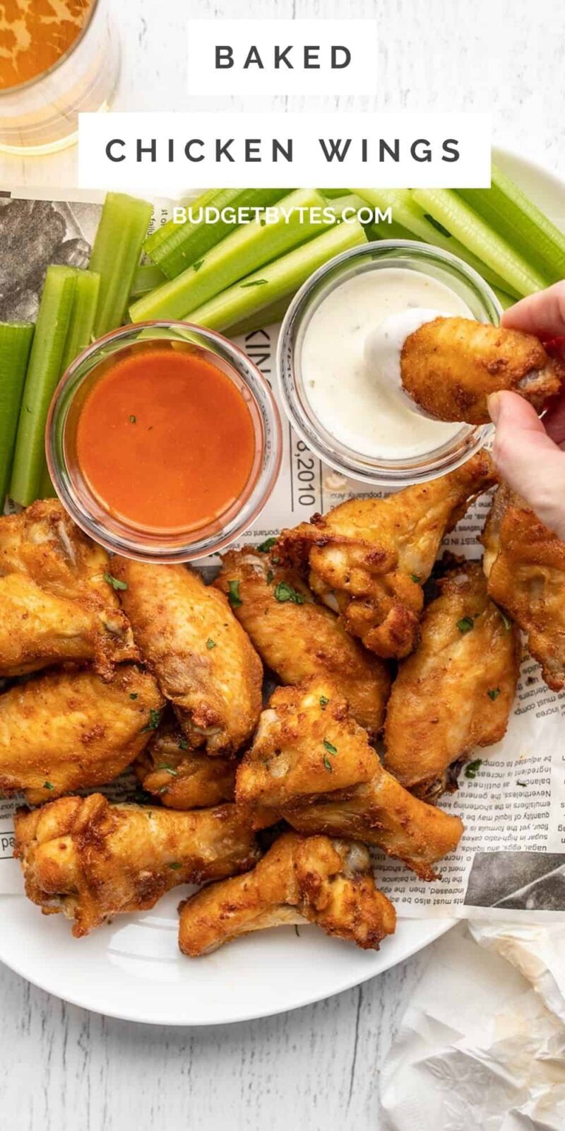 A hand dipping a chicken wing into a bowl of sauce on a platter