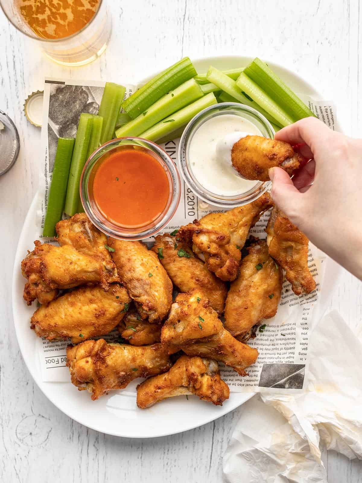 A hand dipping a chicken wing into a bowl of ranch on a platter