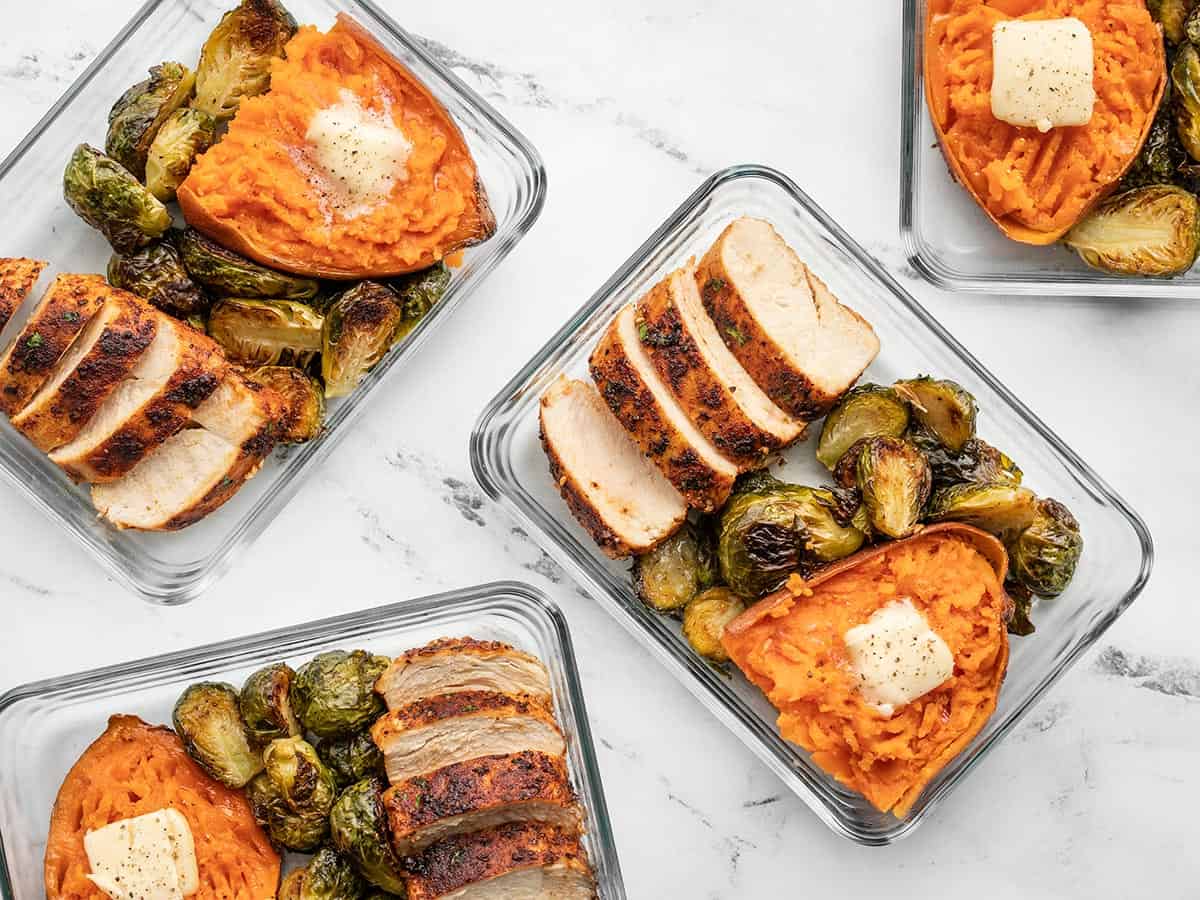 meal prep containers full of chicken, Brussels sprouts, and sweet potato scattered on the surface