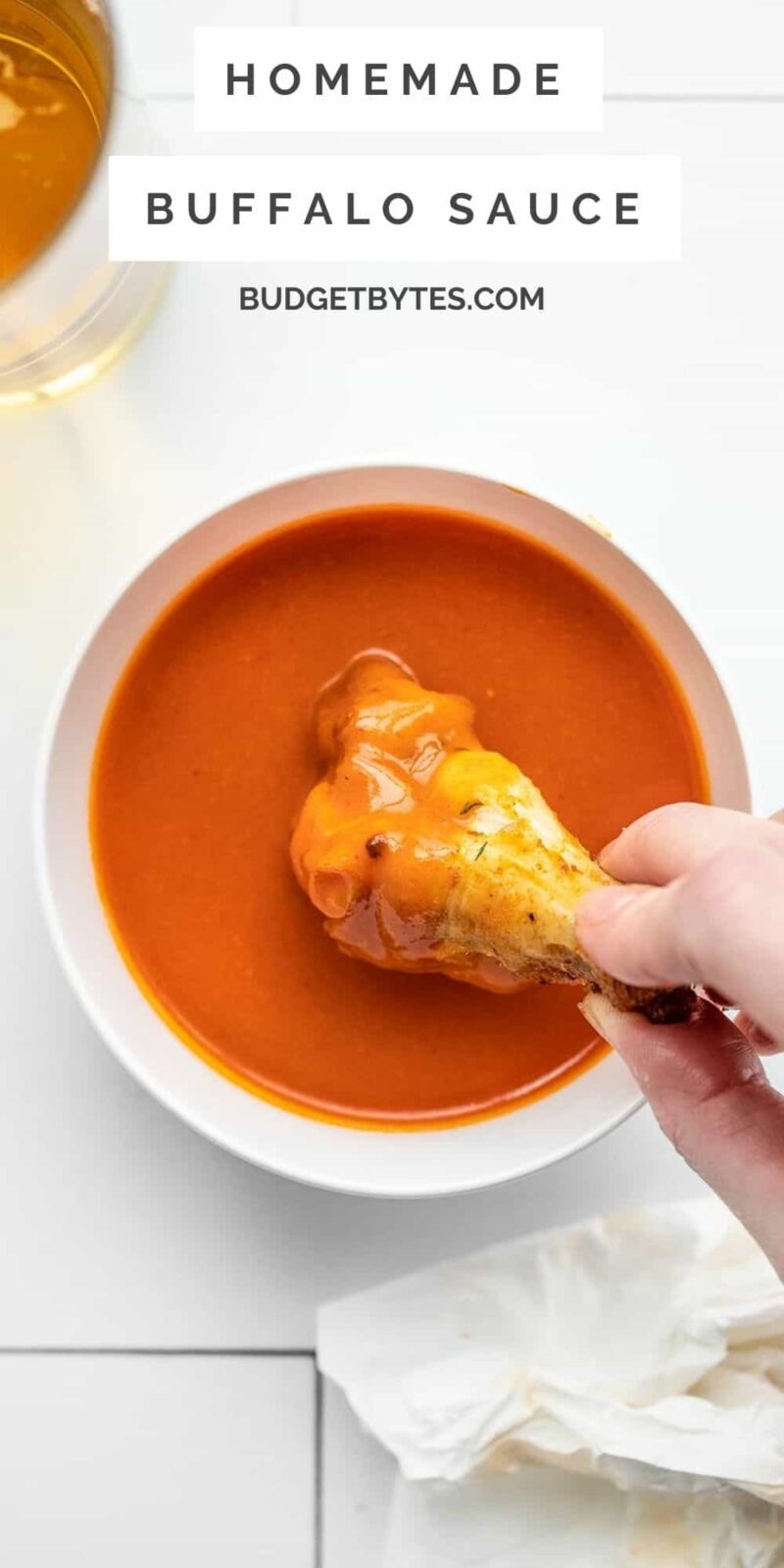 a hand dipping a chicken wing into a bowl of buffalo sauce
