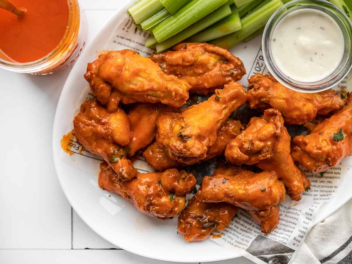 Buffalo wings on a plate with celery next to a jar of buffalo sauce