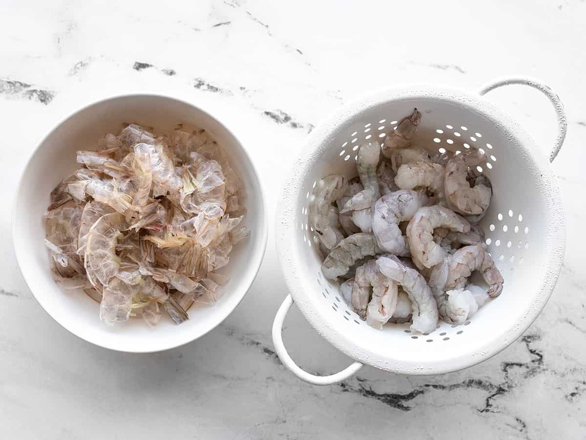 peeled shrimp in a colander next to a bowl of shrimp peels