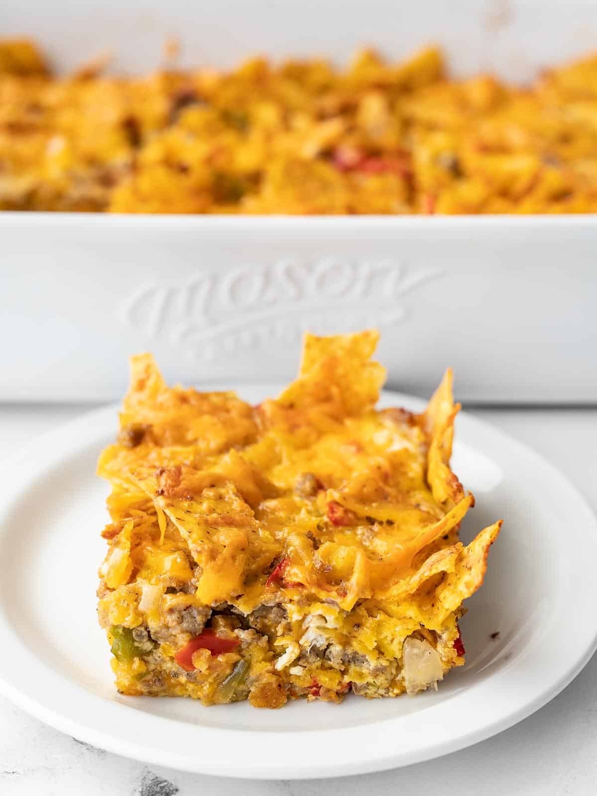 A slice of breakfast casserole on a plate in front of the casserole dish