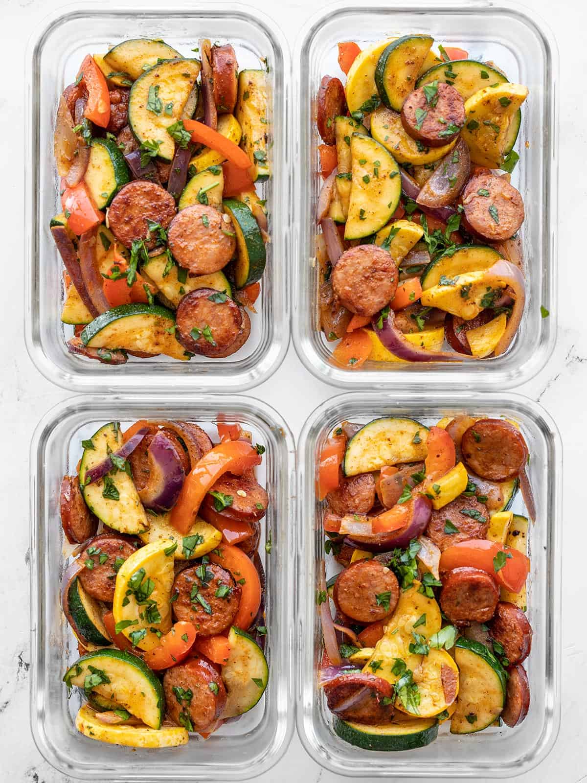 four glass containers full of Cajun sausage and vegetables