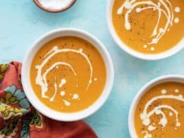 Three bowls of creamy sweet potato soup on a blue background