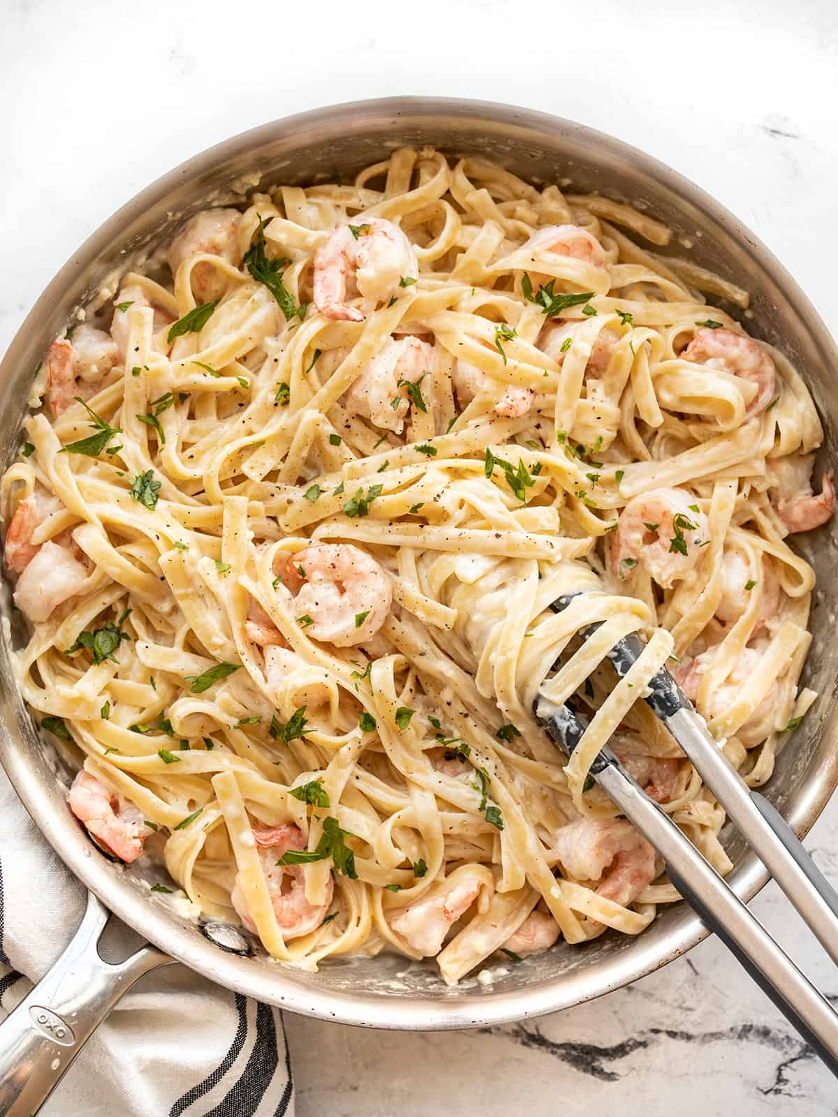 Shrimp alfredo pasta in the skillet with tongs twirling the pasta
