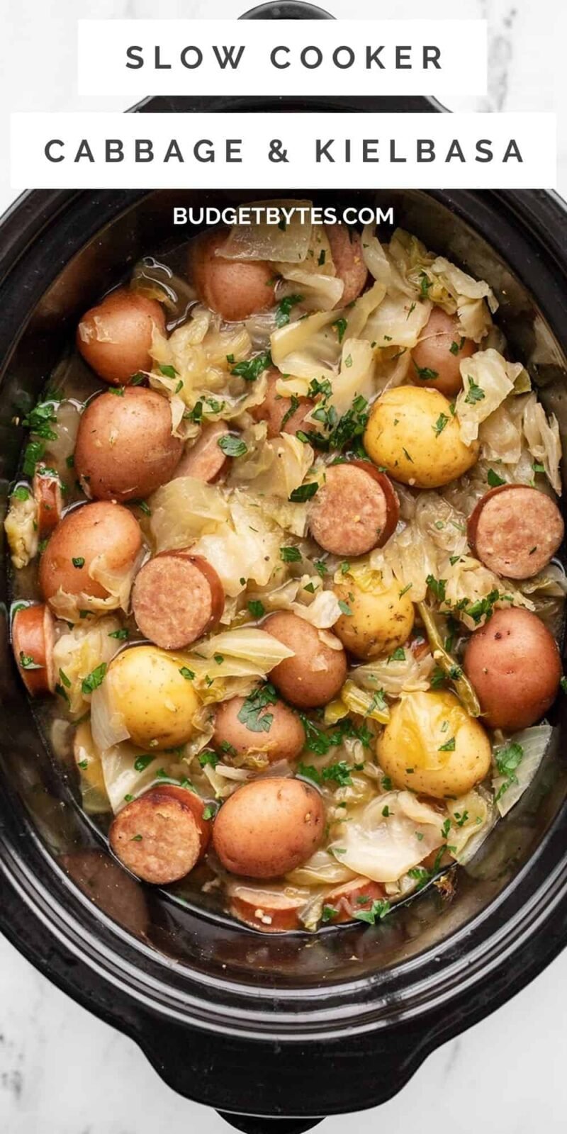 Overhead view of cabbage, sausage, and potatoes in the slow cooker, title text at the top
