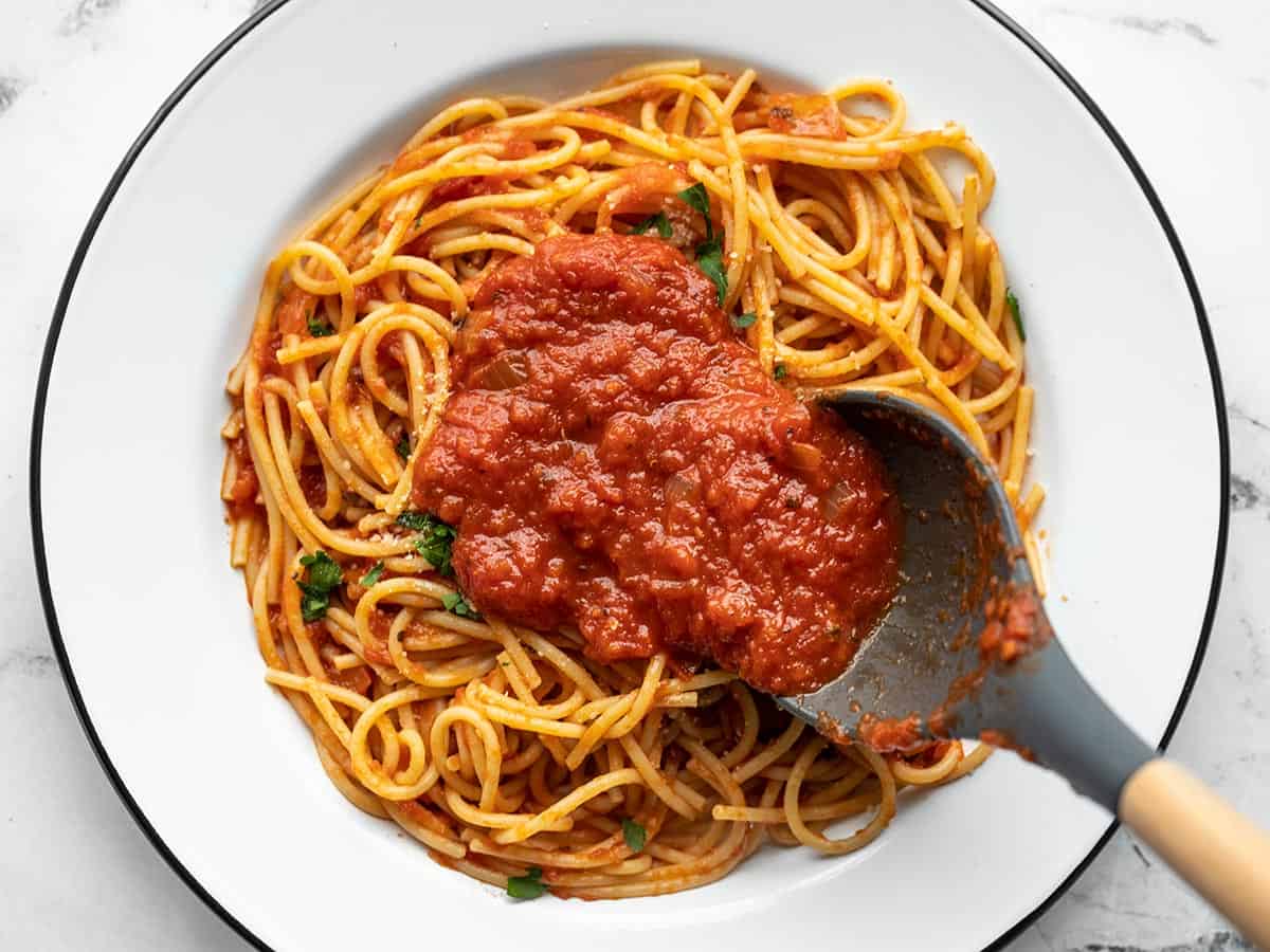 Homemade pasta sauce being spooned over a plate of spaghetti