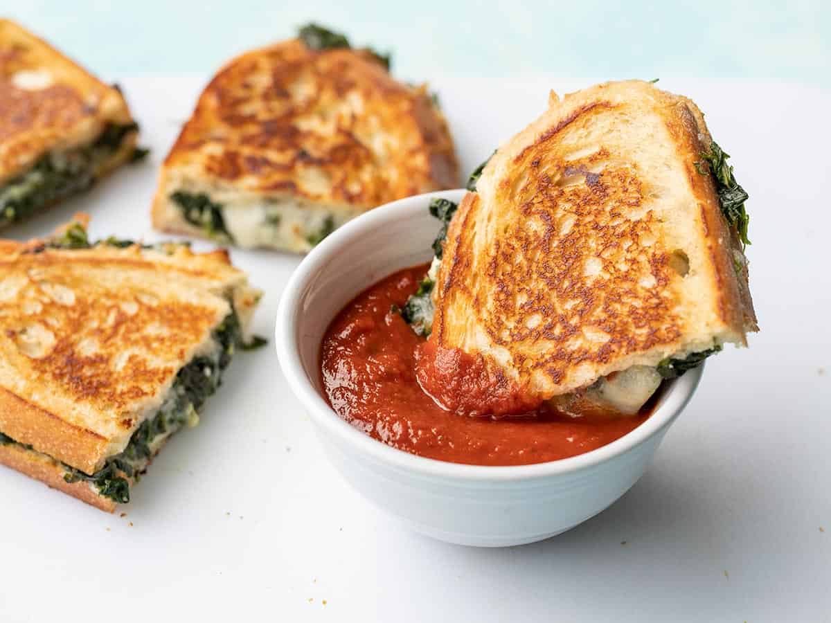Half of a spinach and feta grilled cheese dipping into pizza sauce