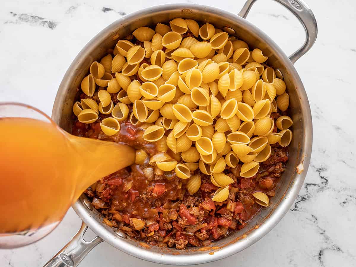 pasta and beef broth being added to the skillet