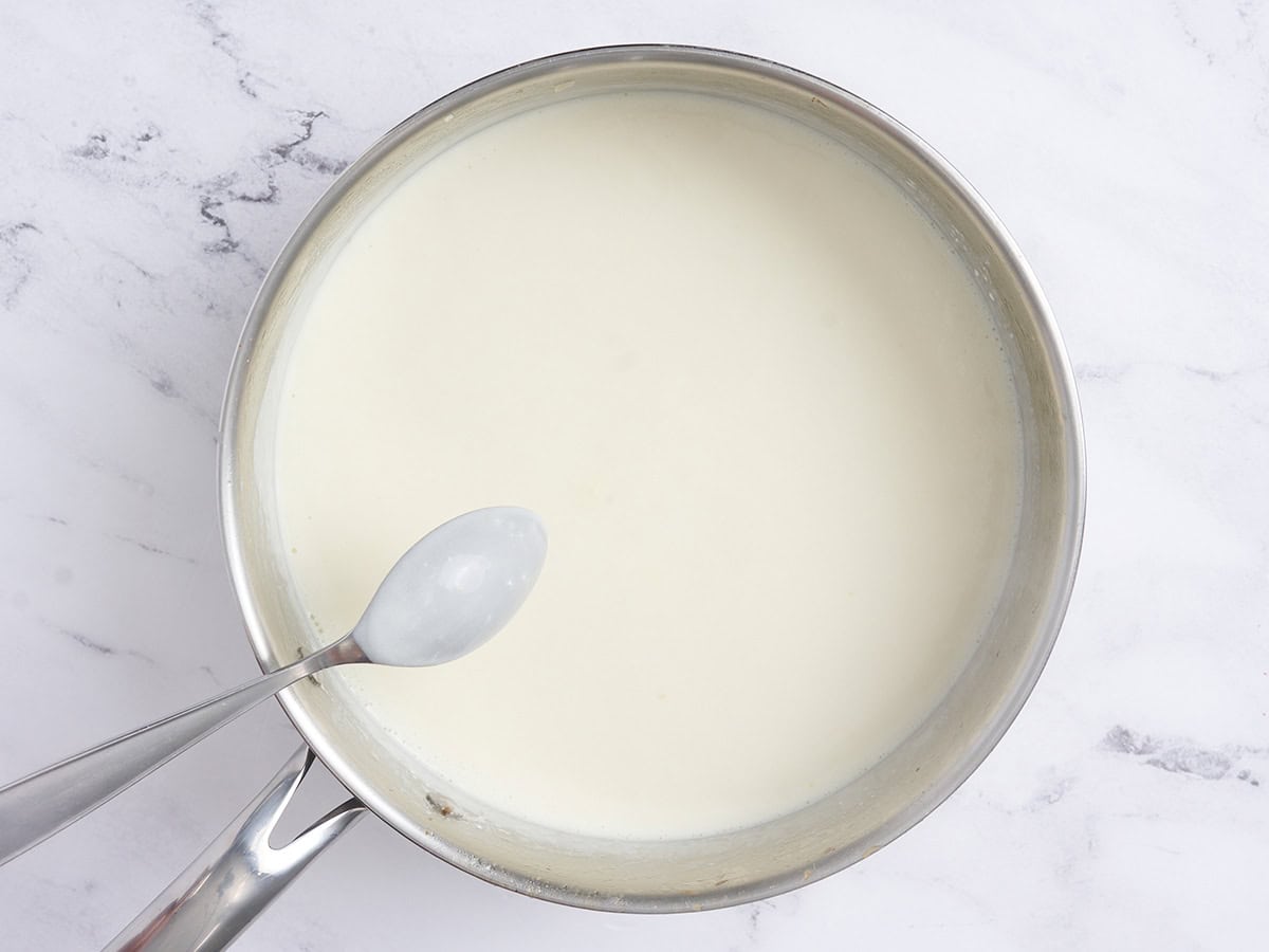 A spoon checking the consistency of the thickned sauce in a skillet.