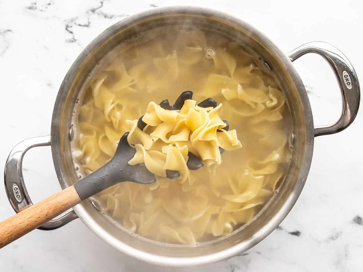 Cooked egg noodles in a pot, pasta spoon in the center