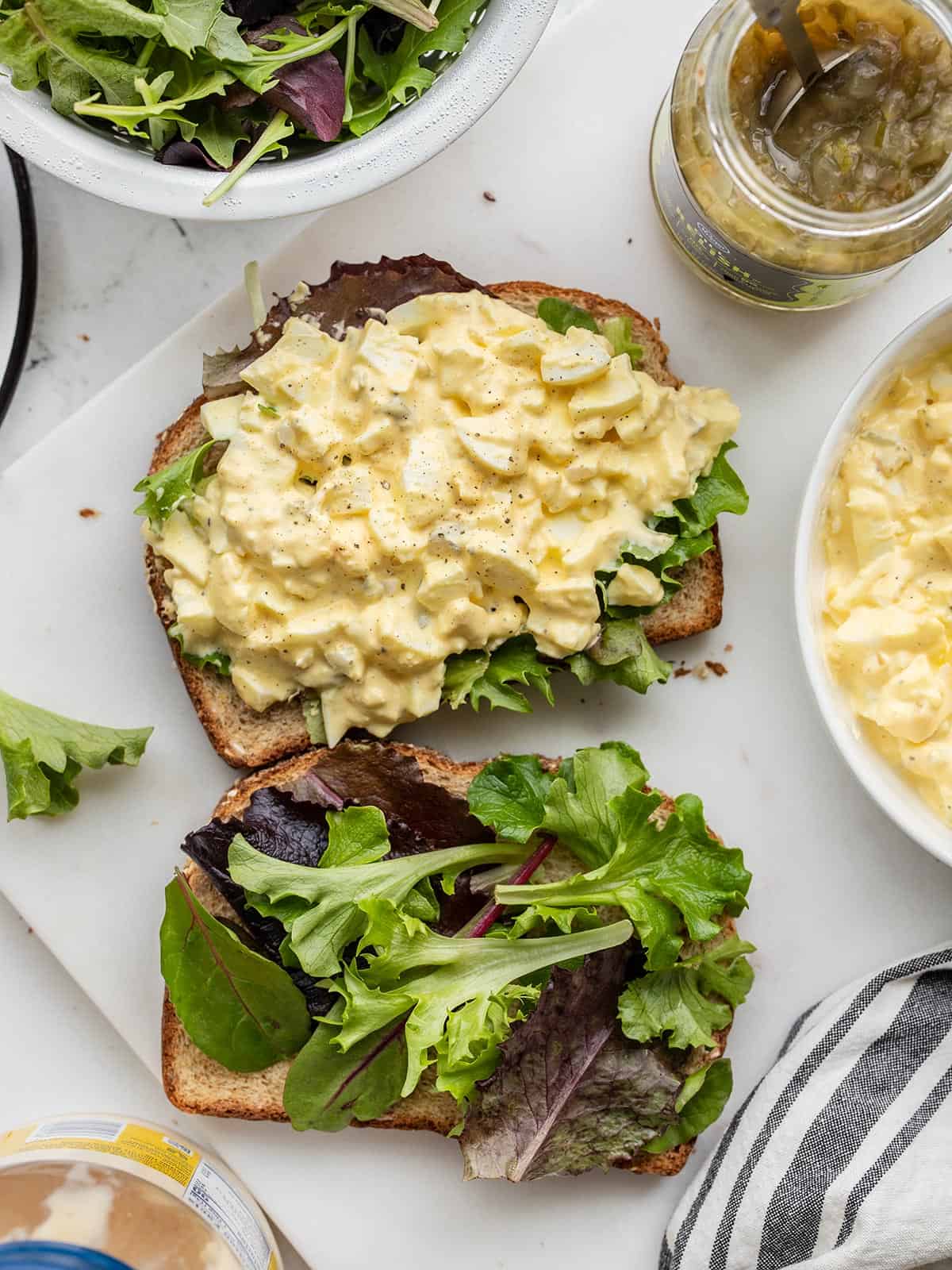 Egg salad on a slice of bread with lettuce and ingredients on the sides