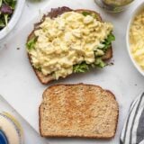 An egg salad sandwich being built on a cutting board
