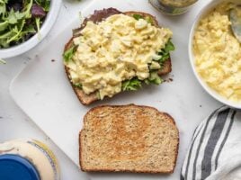 An egg salad sandwich being built on a cutting board