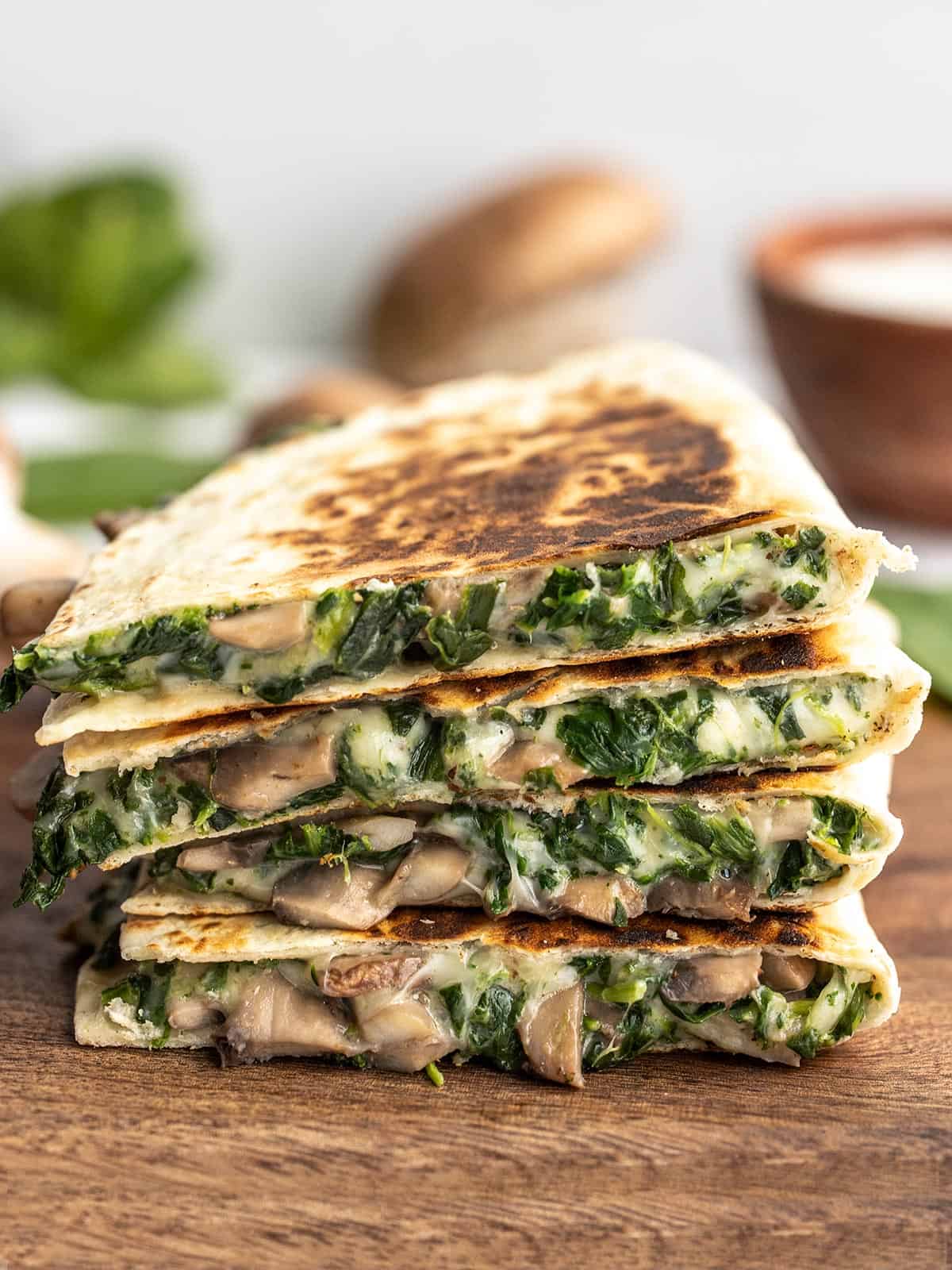 A stack of spinach and mushroom quesadillas on a wooden cutting board