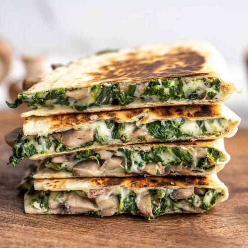 A stack of spinach and mushroom quesadillas on a wooden cutting board