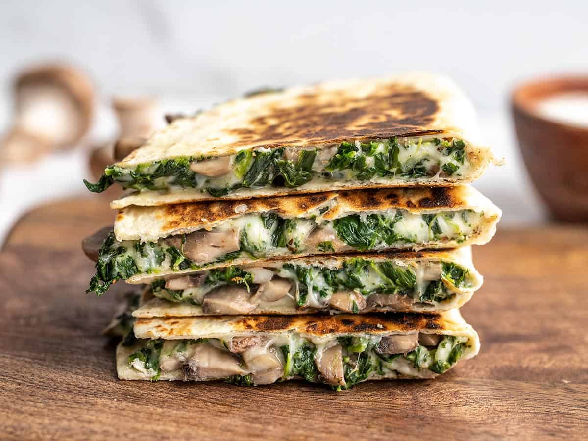 A stack of spinach and mushroom quesadillas on a wooden cutting board