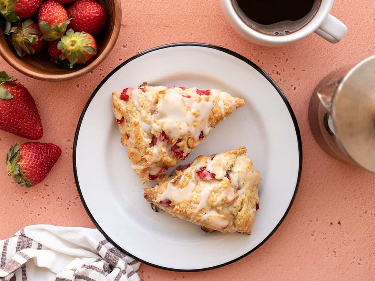 Two strawberry scones on a plate with coffee and a bowl of berries on the side