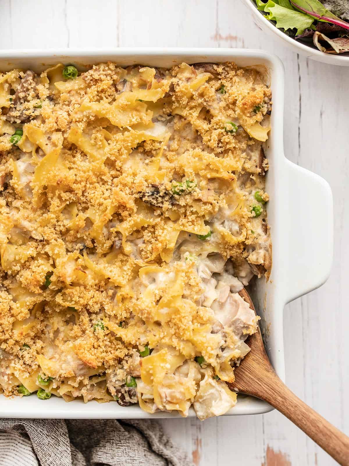 Overhead view of tuna noodle casserole in a square dish with a wooden spoon