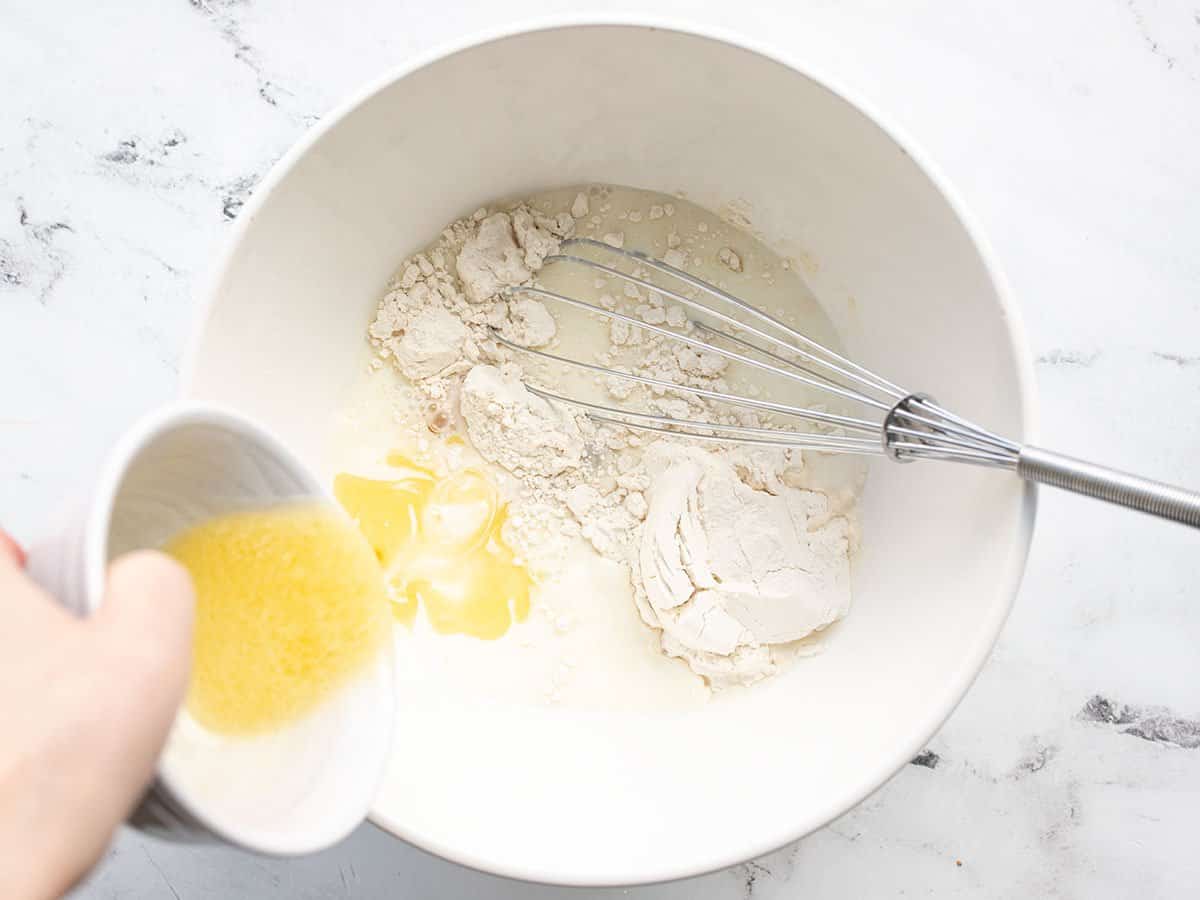 Melted butter being poured into the bowl of crepe batter ingredients.