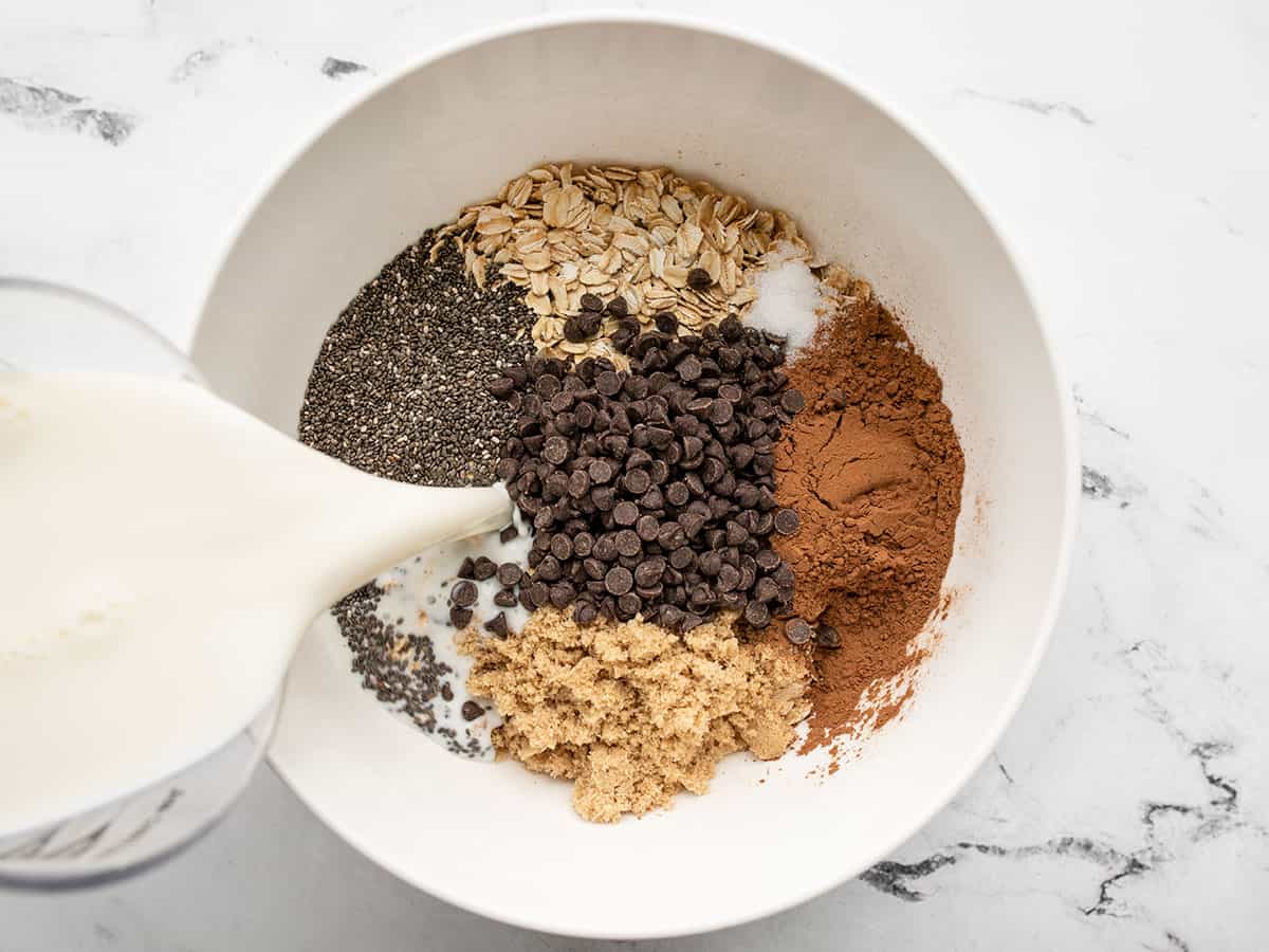 Overnight oats ingredients in a bowl, milk being poured on top.