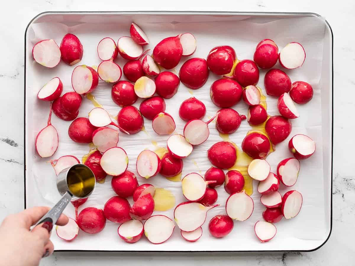 oil being drizzled over the radishes on a baking sheet.
