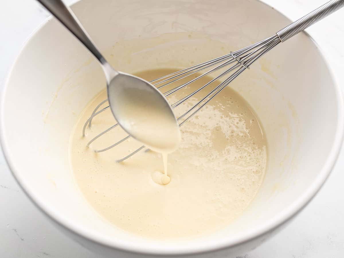 crepe batter dripping off the spoon into the bowl.