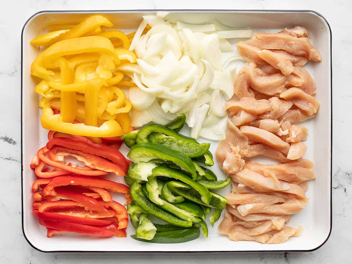 Sliced onions, peppers, and chicken on a baking sheet