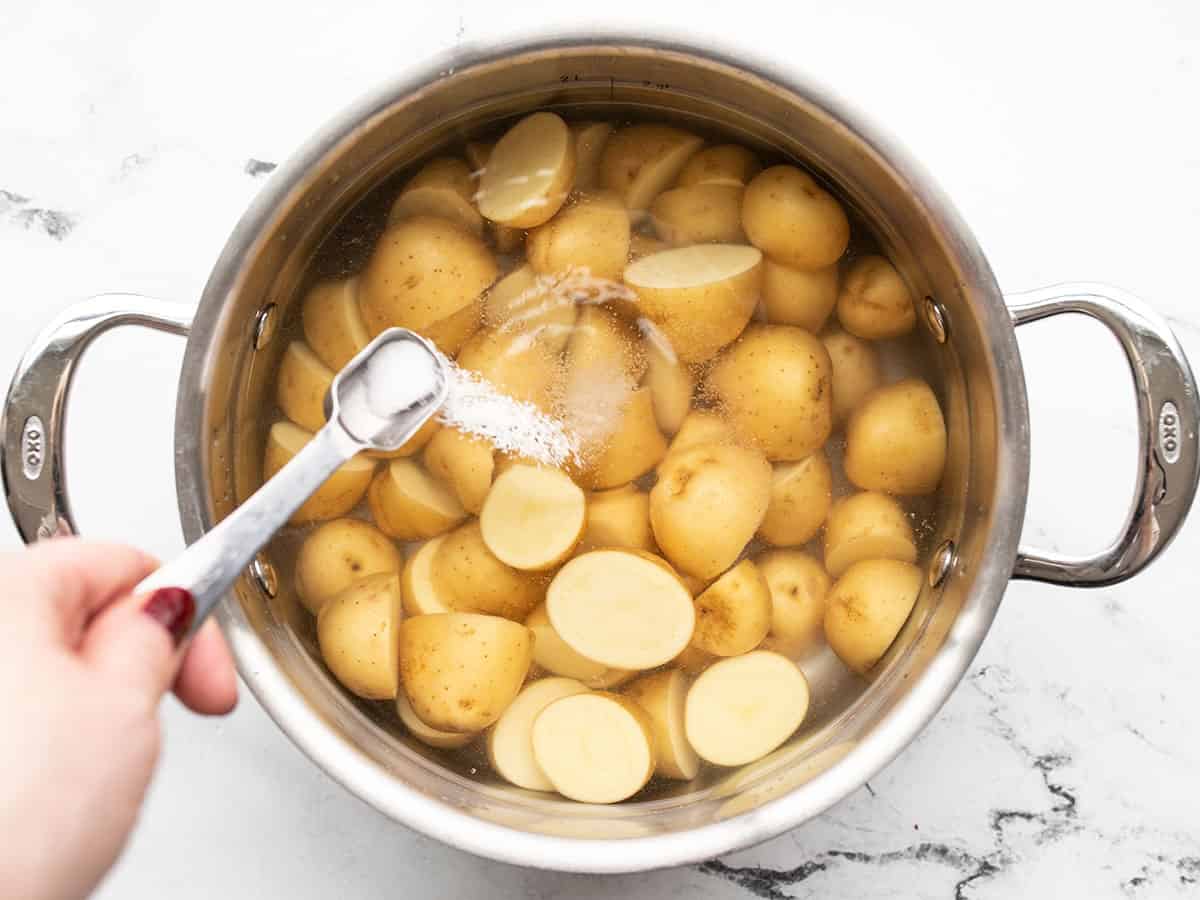 Salt being sprinkled into a pot with potatoes and water.