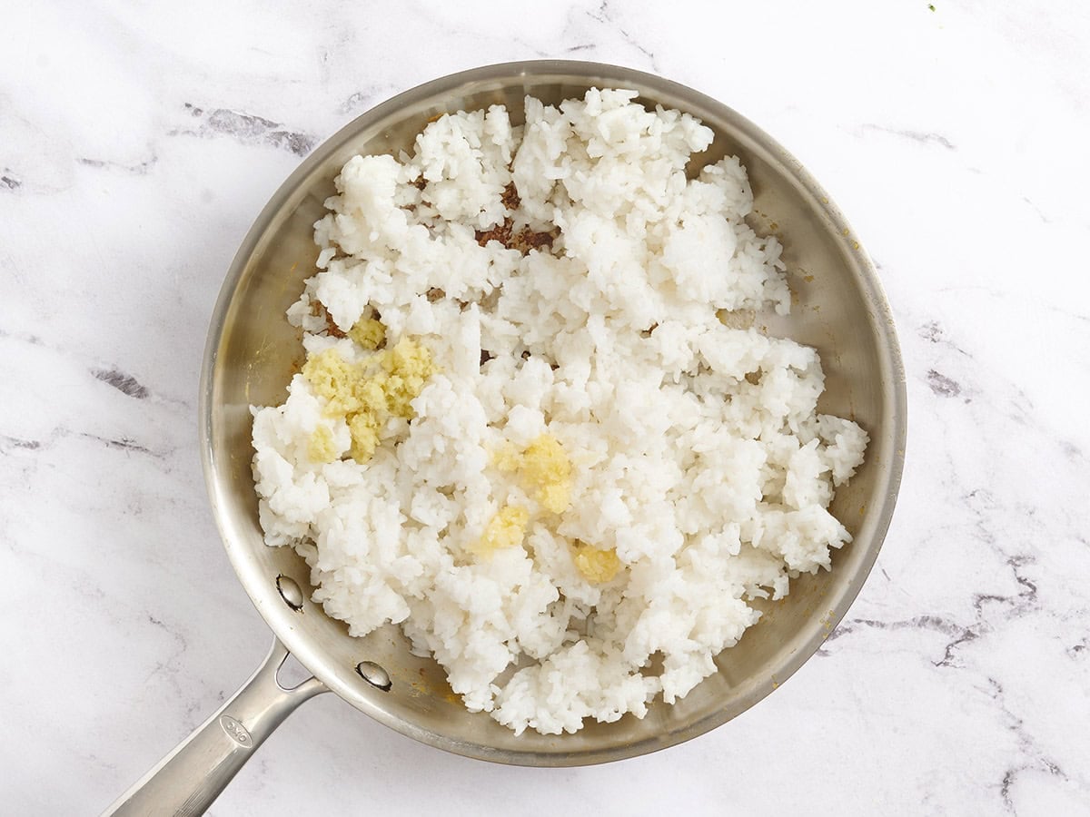 Ginger and garlic added to a skillet with rice.