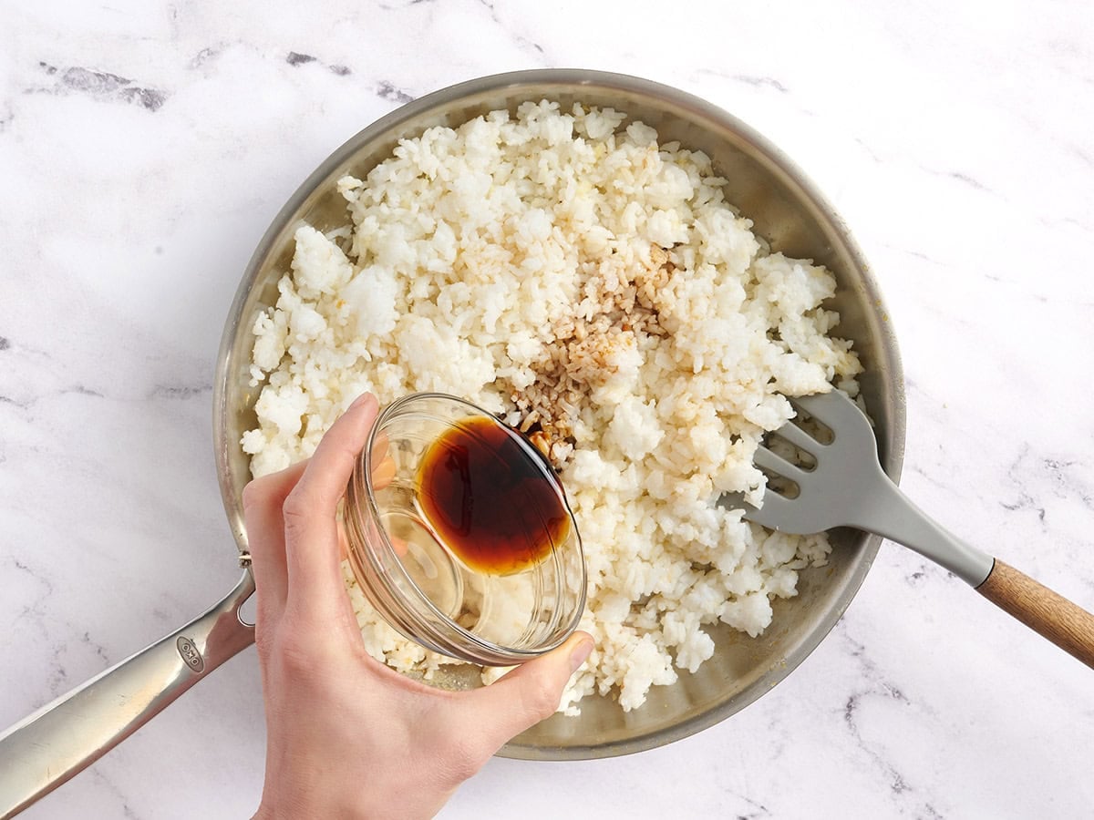 Sesame oil and soy sauce added to a skillet of rice.