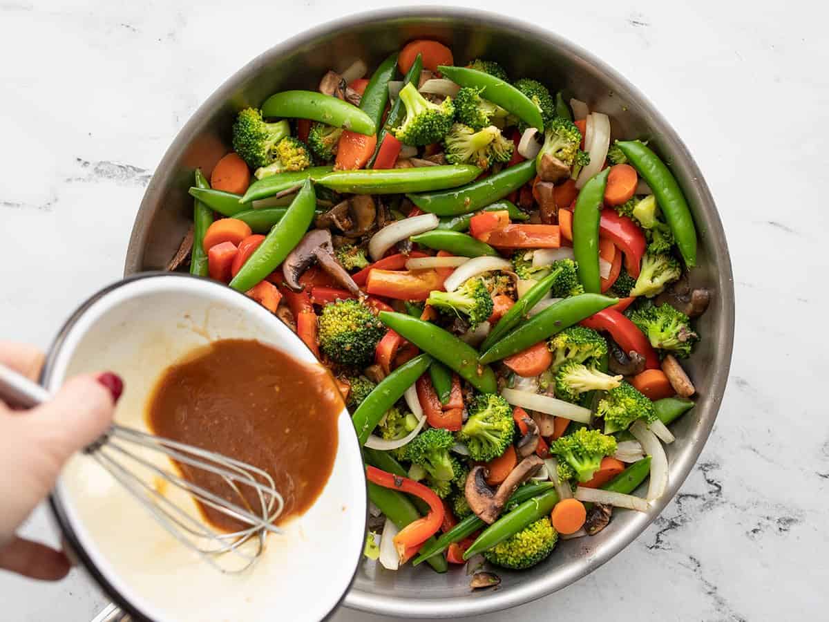 stir fry sauce being poured over the vegetables in the skillet.